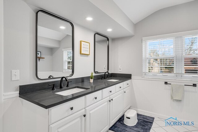 bathroom with lofted ceiling, double vanity, a sink, and tile patterned floors