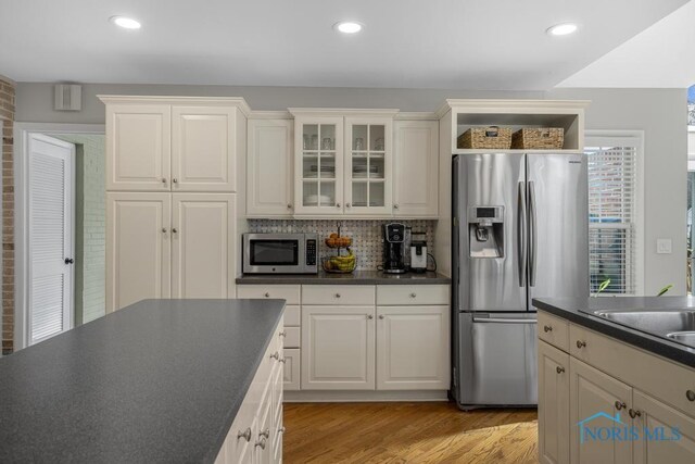 kitchen featuring dark countertops, light wood-style flooring, stainless steel appliances, and decorative backsplash