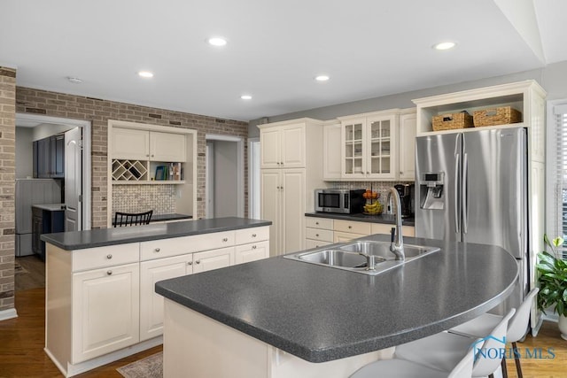 kitchen featuring appliances with stainless steel finishes, dark countertops, a sink, and a kitchen island with sink