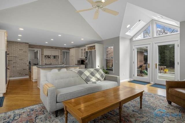 living room featuring high vaulted ceiling, light wood-type flooring, brick wall, and recessed lighting