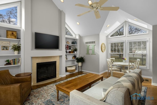 living area featuring a wealth of natural light, a fireplace with flush hearth, built in shelves, and wood finished floors