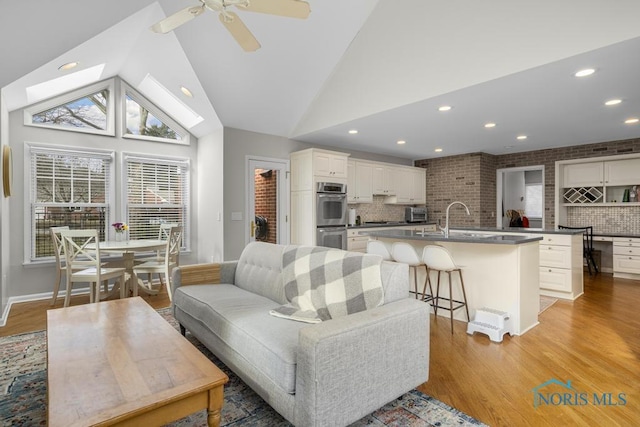 living area featuring light wood-style floors, ceiling fan, high vaulted ceiling, and recessed lighting