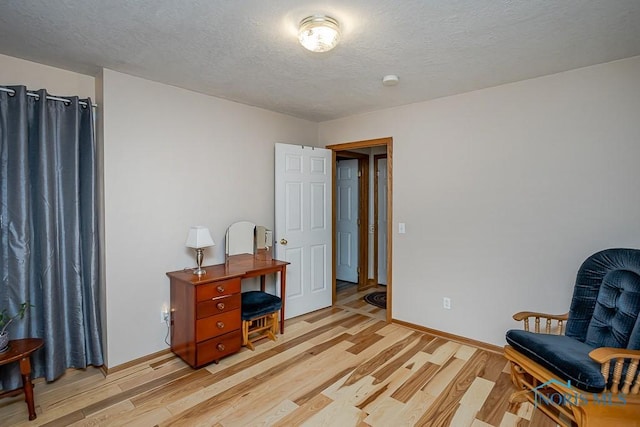 sitting room featuring light wood-style floors, a textured ceiling, and baseboards