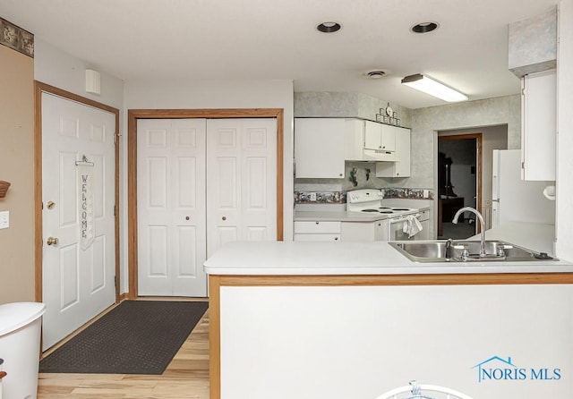 kitchen featuring light countertops, white cabinets, a sink, white appliances, and a peninsula