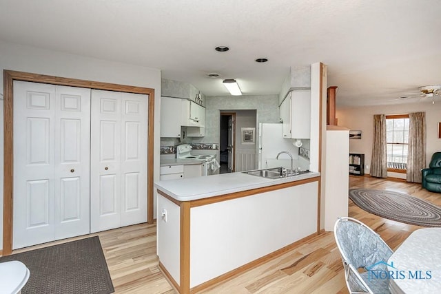 kitchen with white range with electric cooktop, light countertops, light wood-style flooring, white cabinetry, and a sink