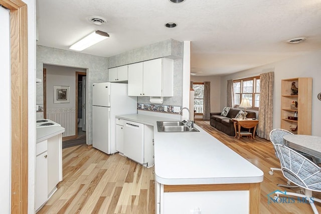 kitchen featuring visible vents, open floor plan, a sink, white appliances, and a peninsula