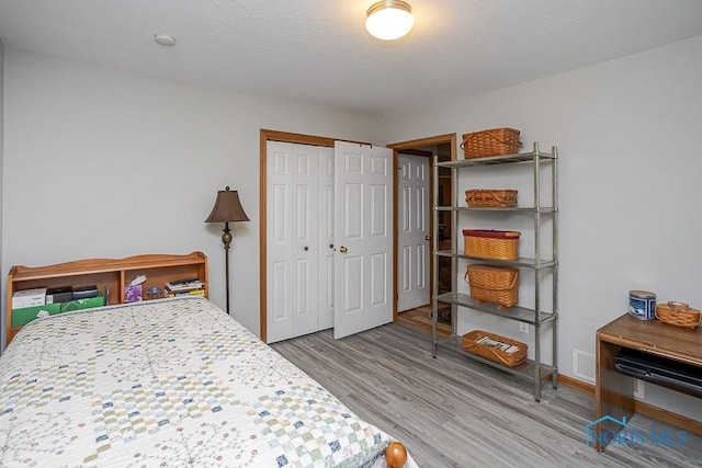 bedroom featuring a closet, visible vents, a textured ceiling, and wood finished floors