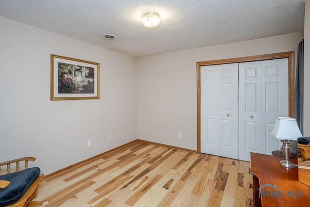 bedroom with light wood finished floors, baseboards, visible vents, a textured ceiling, and a closet