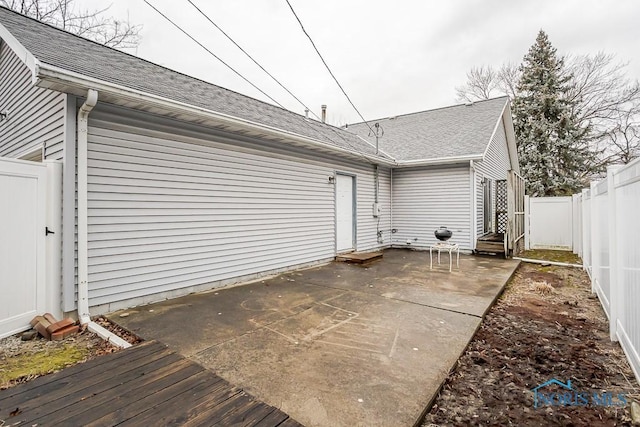 rear view of house with entry steps, roof with shingles, a patio area, and a fenced backyard