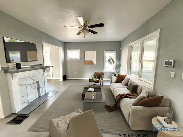 living room featuring a fireplace, visible vents, a ceiling fan, a textured ceiling, and baseboards