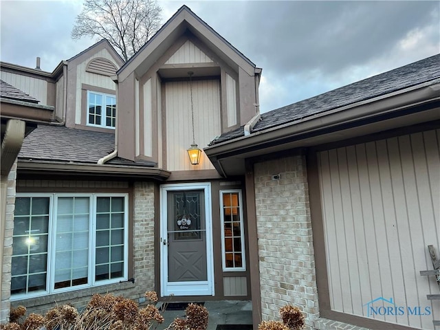 view of exterior entry featuring roof with shingles and brick siding