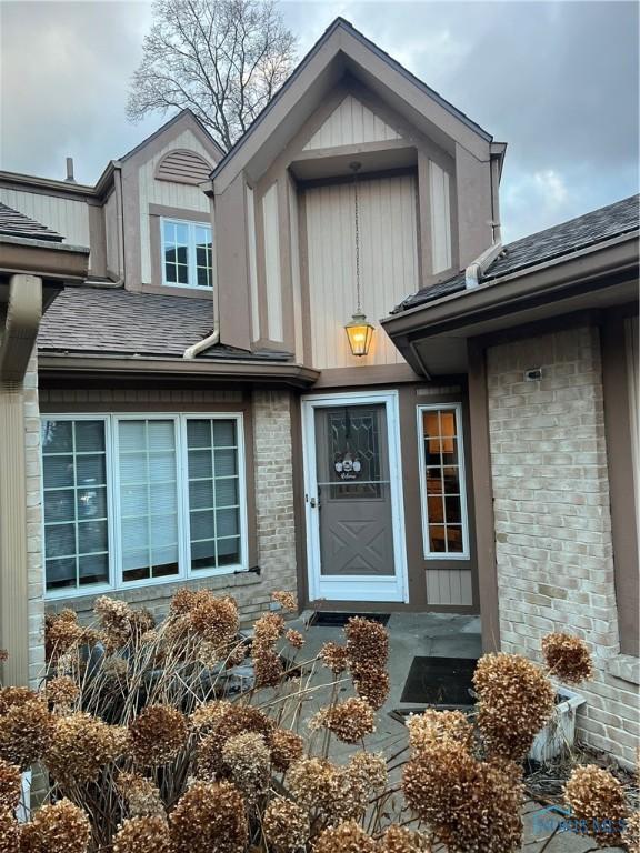 property entrance with a shingled roof and brick siding