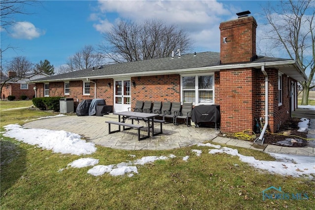 back of property featuring a chimney, a lawn, a patio, and brick siding