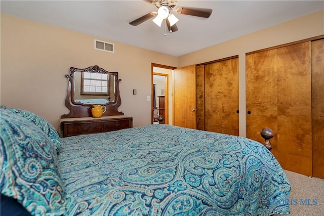 carpeted bedroom featuring multiple closets, visible vents, and a ceiling fan