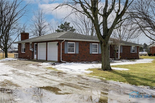 snow covered property with an attached garage, driveway, a chimney, and brick siding