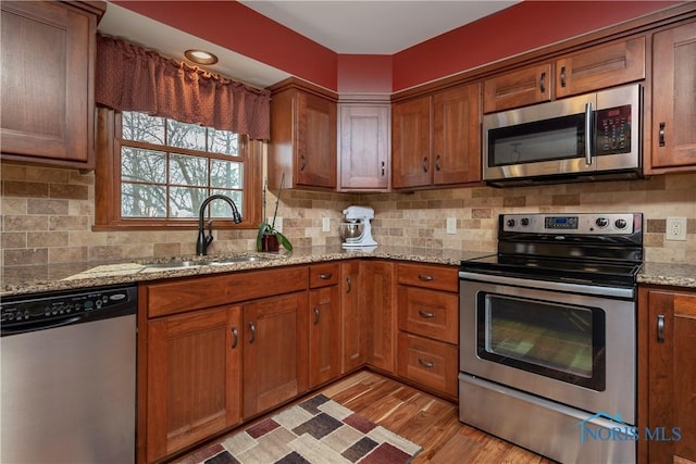 kitchen featuring brown cabinets, stainless steel appliances, backsplash, light wood-style floors, and a sink