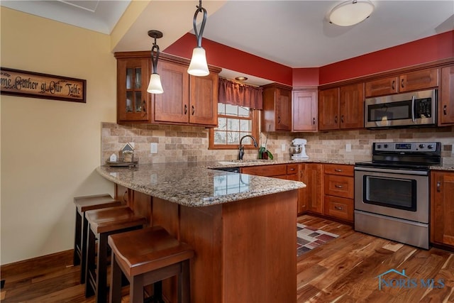 kitchen featuring dark wood finished floors, a breakfast bar, a peninsula, stainless steel appliances, and a sink