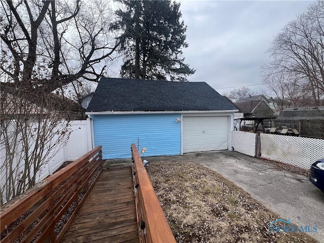 detached garage featuring concrete driveway and fence