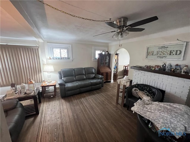 living room featuring dark wood-style floors, ceiling fan, a fireplace, and arched walkways