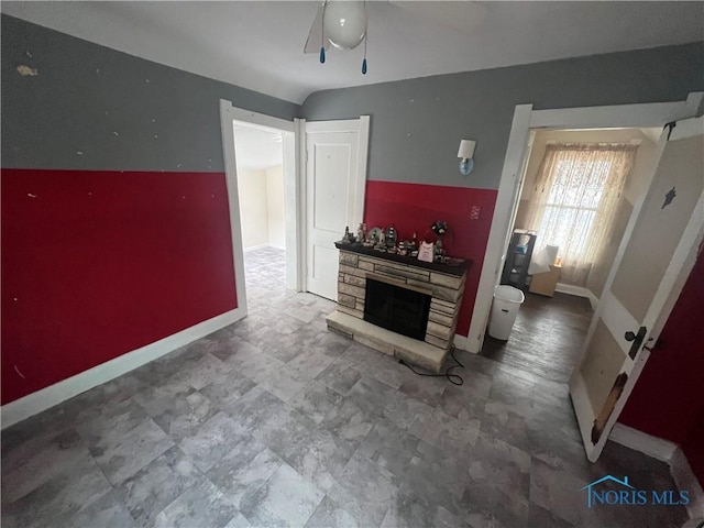 living room featuring ceiling fan, a fireplace, and baseboards