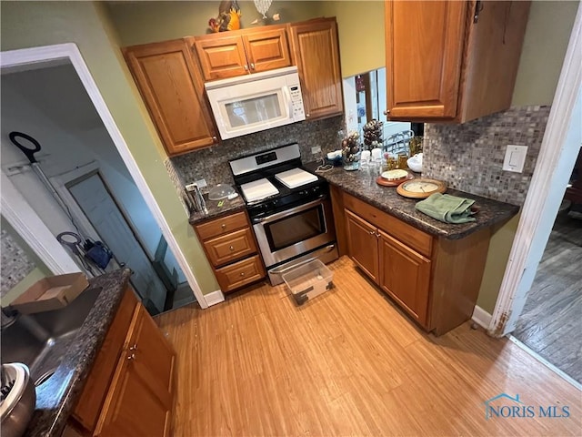 kitchen with white microwave, stainless steel gas range oven, brown cabinets, light wood finished floors, and tasteful backsplash