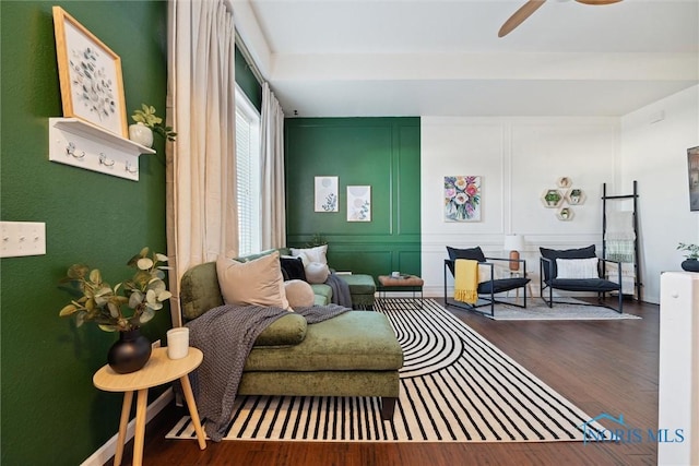 sitting room with a ceiling fan, a decorative wall, and wood finished floors