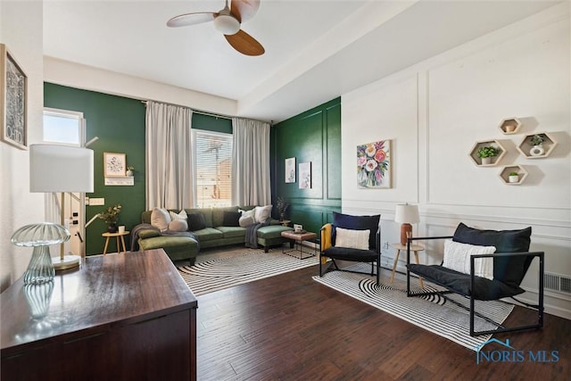 living area with visible vents, a ceiling fan, a decorative wall, and wood finished floors