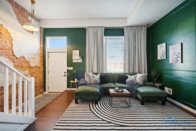 living area featuring brick wall, visible vents, baseboards, stairs, and dark wood finished floors