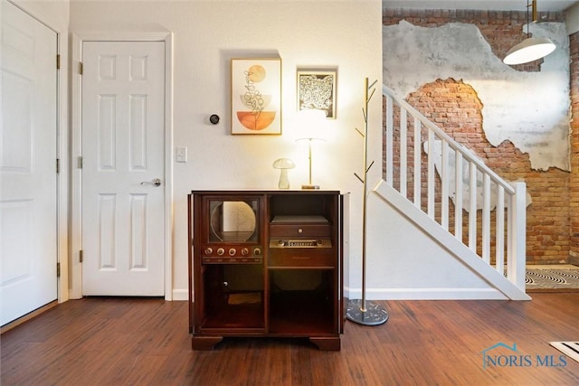 interior space with baseboards, stairway, brick wall, and wood finished floors