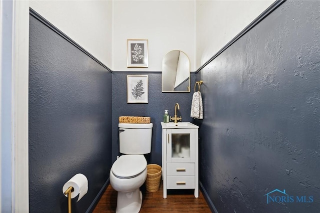 half bath with a textured wall, wood finished floors, a sink, and toilet