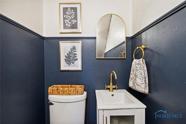 half bath with toilet, a textured wall, and vanity