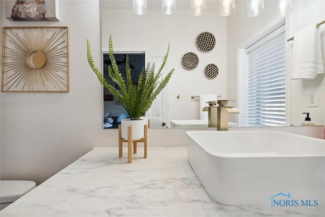 bathroom featuring toilet, marble finish floor, a sink, and a freestanding bath