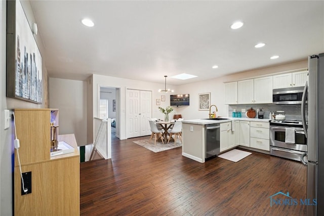 kitchen with dark wood-style floors, a peninsula, stainless steel appliances, light countertops, and a sink