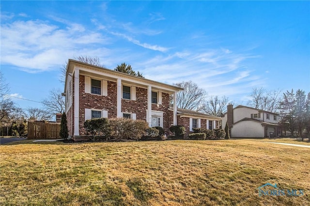 greek revival house featuring brick siding, a front yard, and fence