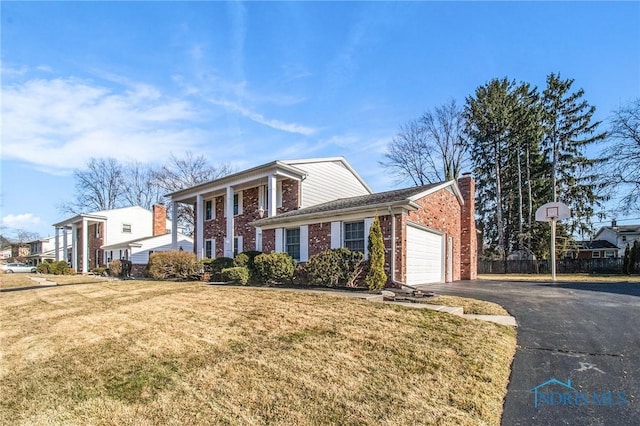 neoclassical home featuring aphalt driveway, an attached garage, a front yard, brick siding, and a chimney