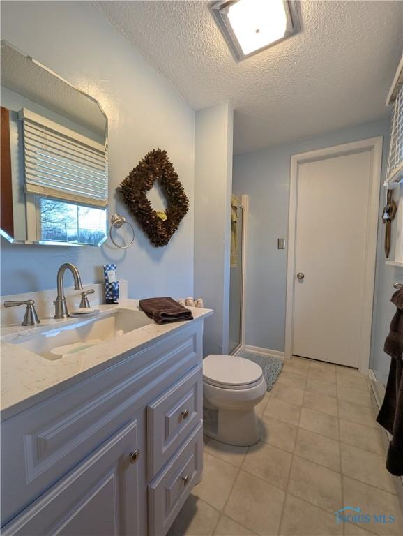 bathroom with toilet, a stall shower, vanity, a textured ceiling, and tile patterned floors