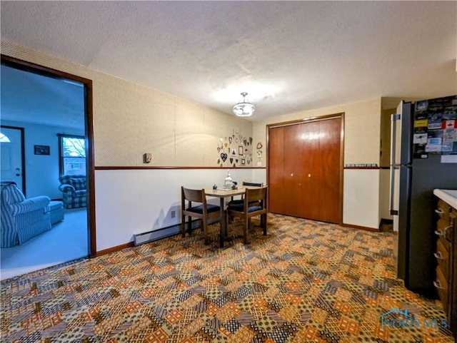 carpeted dining area with a textured ceiling, baseboard heating, and baseboards