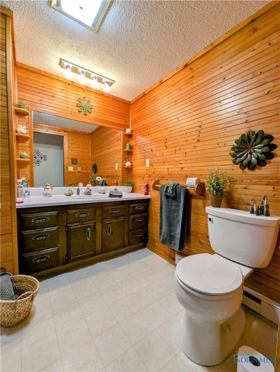 bathroom featuring a textured ceiling, a baseboard radiator, toilet, wood walls, and vanity