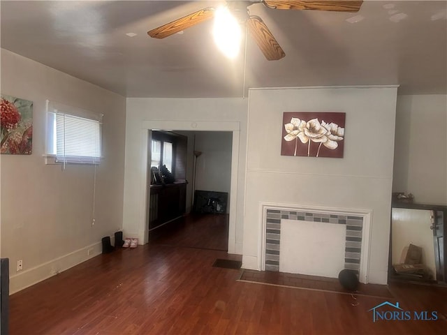 unfurnished living room featuring ceiling fan, a tiled fireplace, baseboards, and wood finished floors