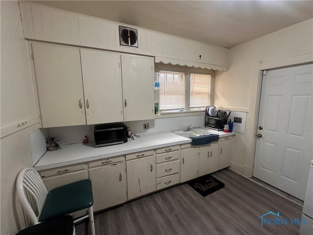 kitchen with dark wood-type flooring, a sink, visible vents, white cabinets, and light countertops