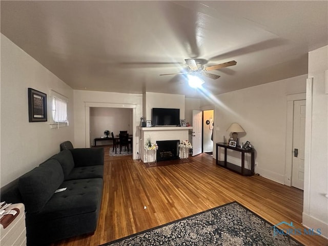 living area with a fireplace with flush hearth, a ceiling fan, baseboards, and wood finished floors