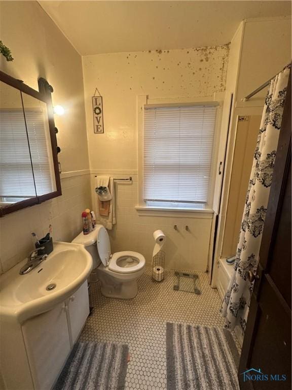 bathroom featuring wainscoting, toilet, tile patterned floors, vanity, and tile walls