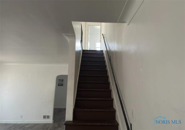 staircase featuring arched walkways, visible vents, baseboards, and wood finished floors