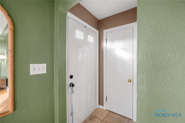 foyer entrance featuring arched walkways, light tile patterned flooring, and a textured wall