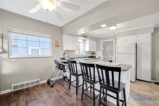 kitchen with baseboards, visible vents, white cabinets, decorative backsplash, and freestanding refrigerator