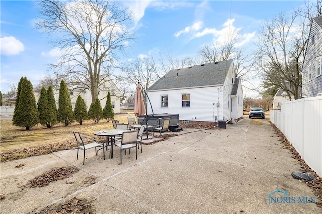 rear view of property with a patio, fence, roof with shingles, outdoor dining space, and a hot tub