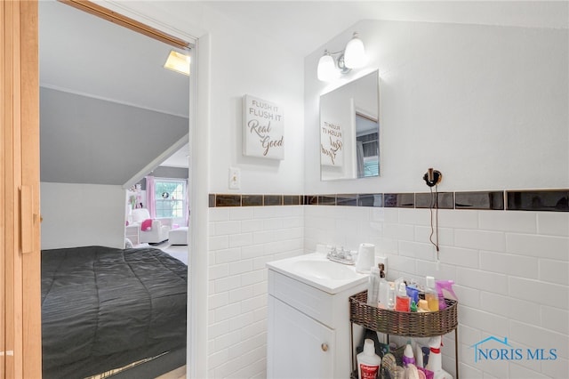 bathroom with lofted ceiling, a wainscoted wall, tile walls, and vanity