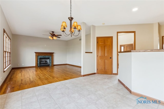 unfurnished living room with a fireplace, light wood-style flooring, baseboards, and ceiling fan with notable chandelier