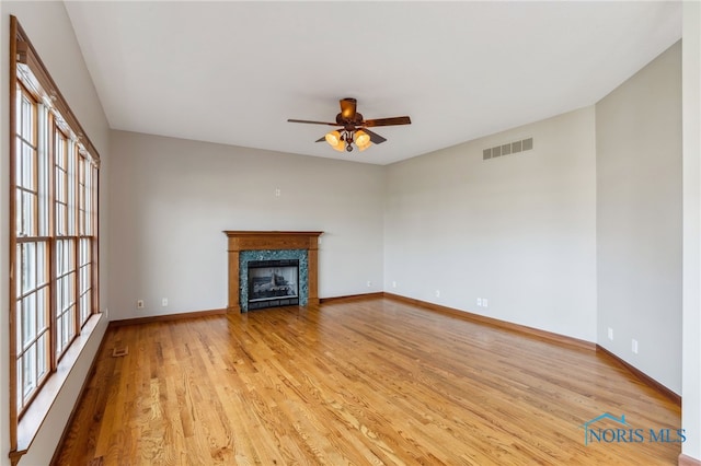 unfurnished living room featuring a fireplace, visible vents, light wood-style floors, ceiling fan, and baseboards