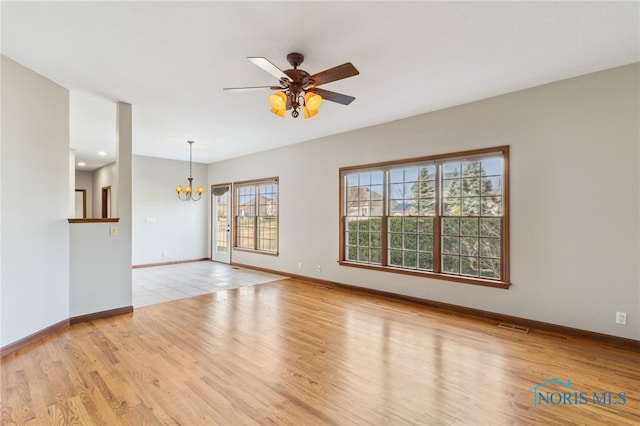 unfurnished room with ceiling fan with notable chandelier, wood finished floors, visible vents, and baseboards